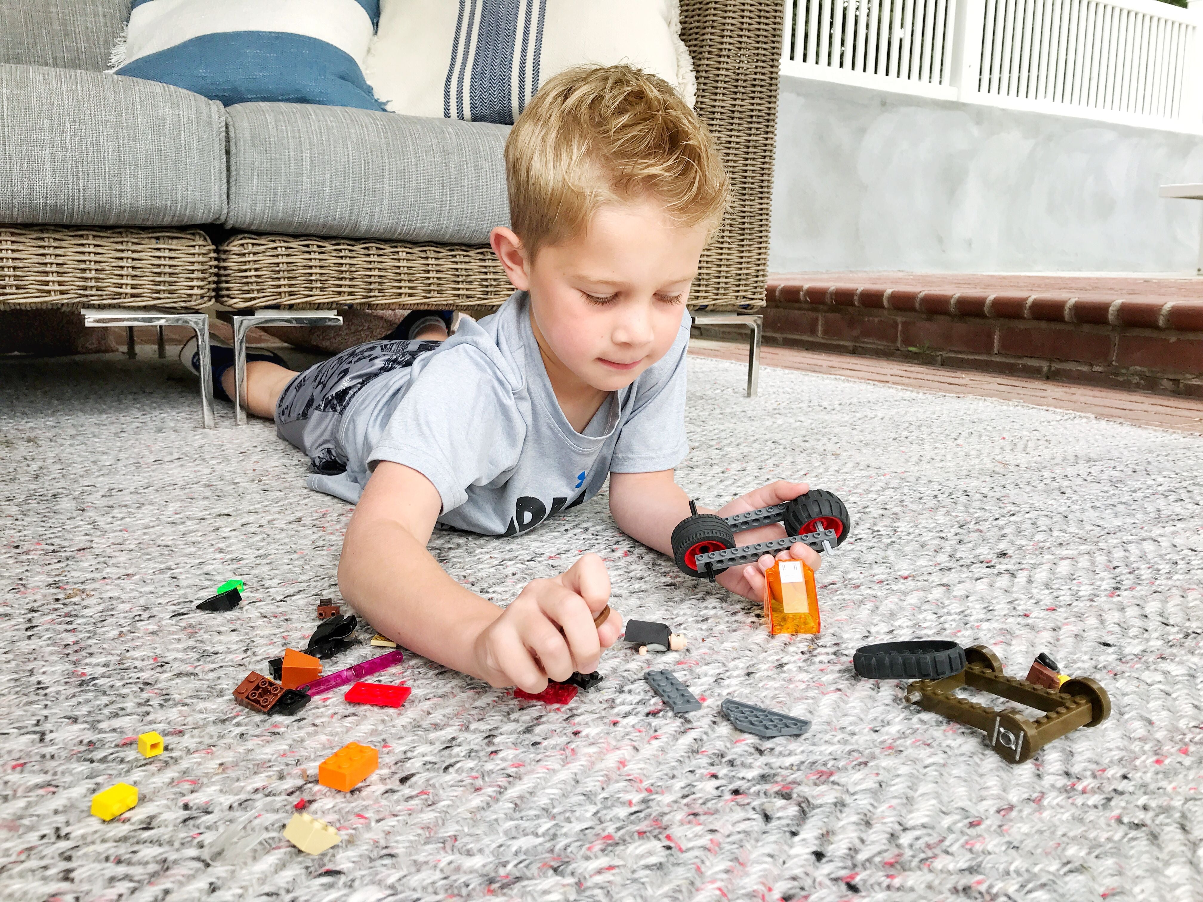 Child playing with toy blocks on an outdoor rug in front of patio seating