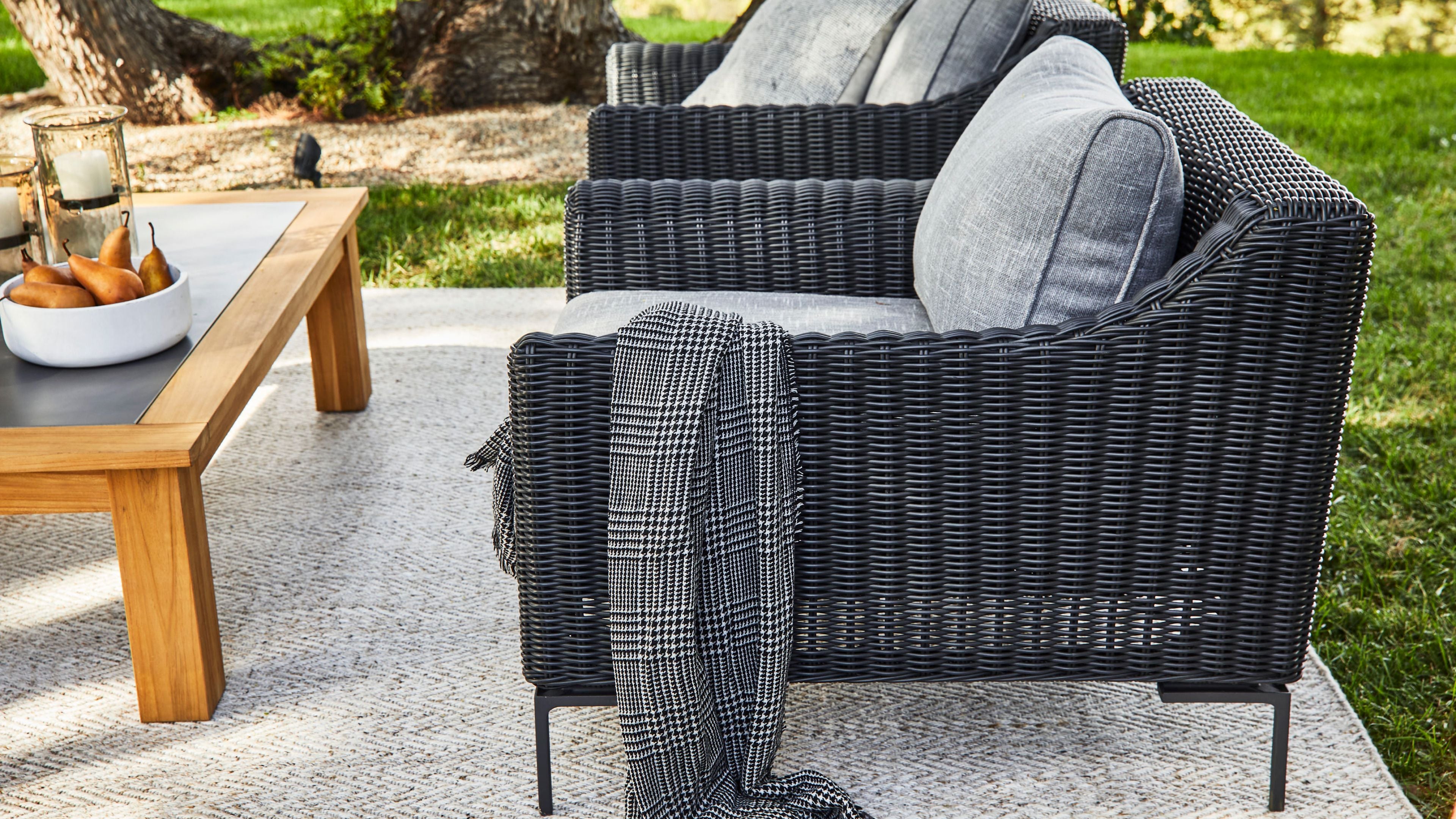 Outdoor wicker armchair with recycled fabric cushions and throw blanket on a patio, featuring weather-resistant seating designed for sustainable outdoor living