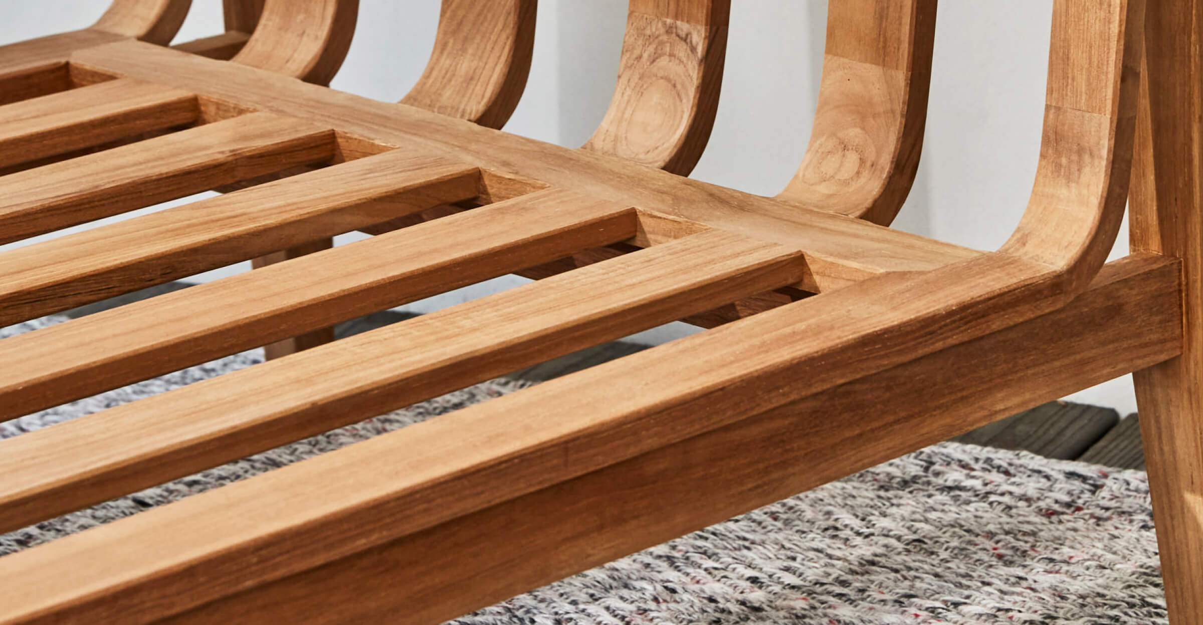 Close-up view of a solid teak wood outdoor bench frame, highlighting natural grain and slatted construction