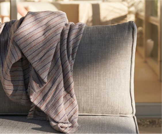 Close-up of soft outdoor upholstery fabric on a cushioned seat with a folded throw blanket, showing texture and stitching detail