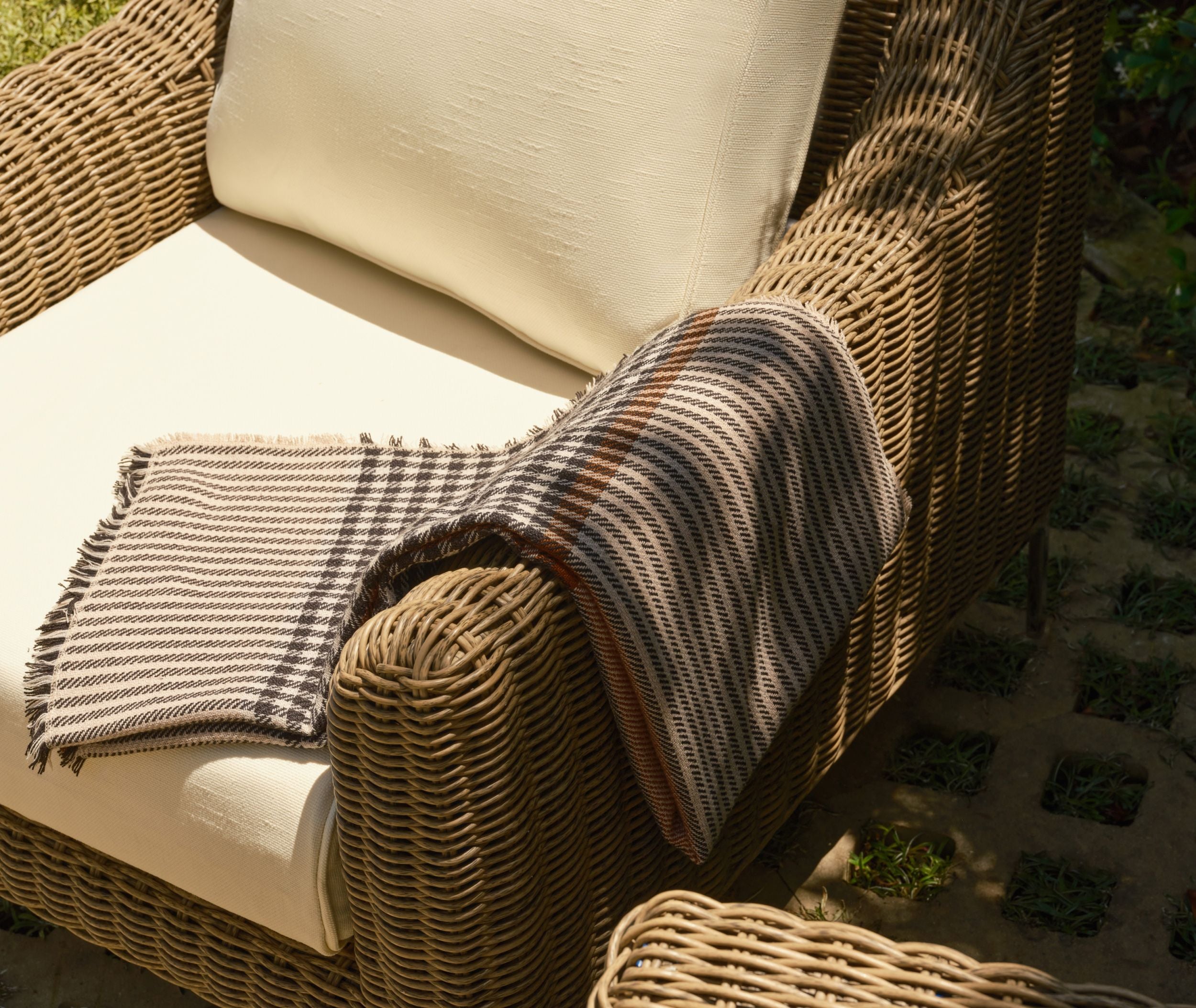 Woven wicker outdoor armchair with cushioned seat and folded throw blanket