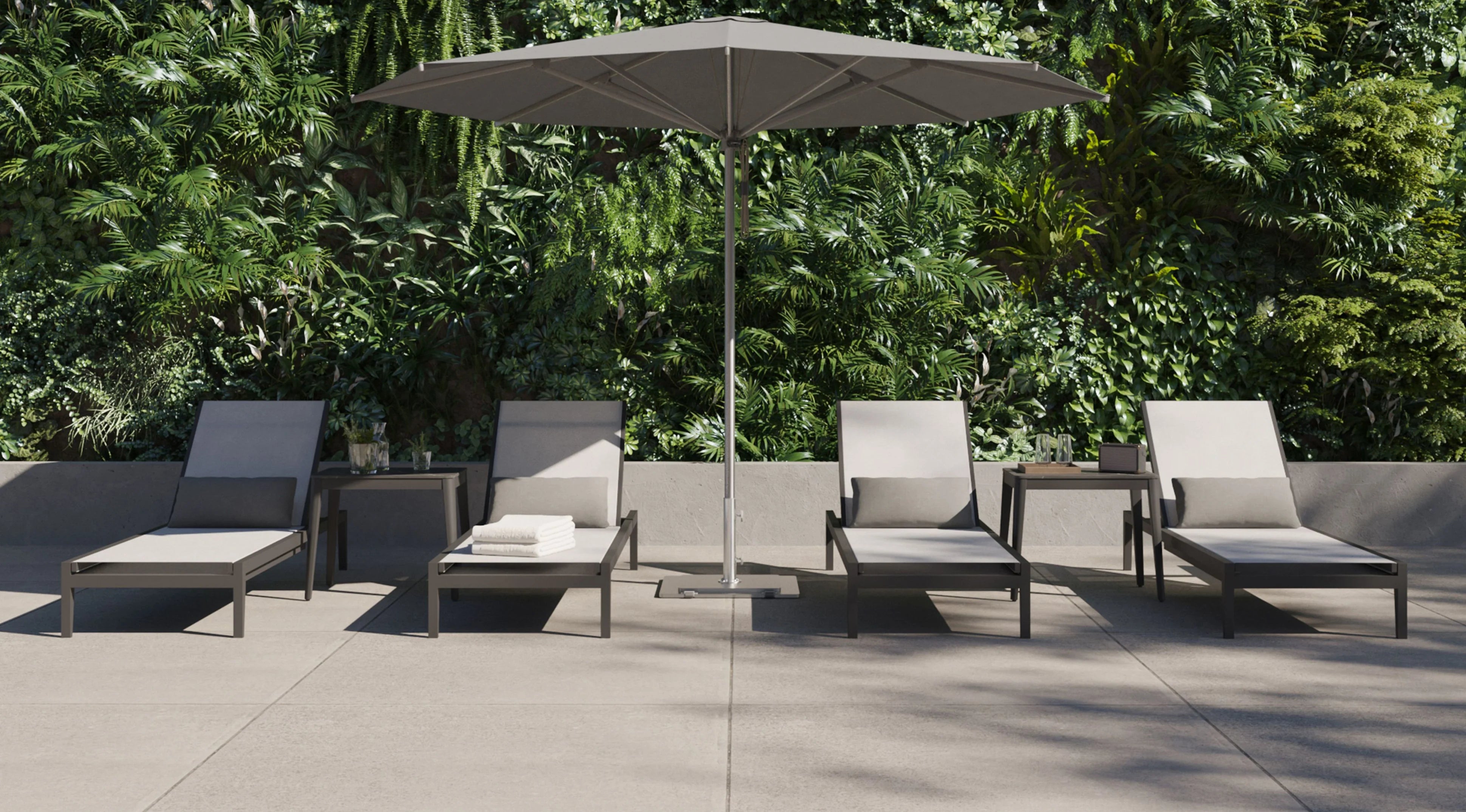 Outdoor chaise lounges with cushions arranged beside side tables under a large patio umbrella