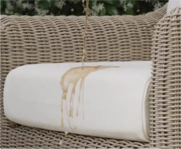 Liquid spilling onto a light-colored fabric cushion on a woven outdoor sofa