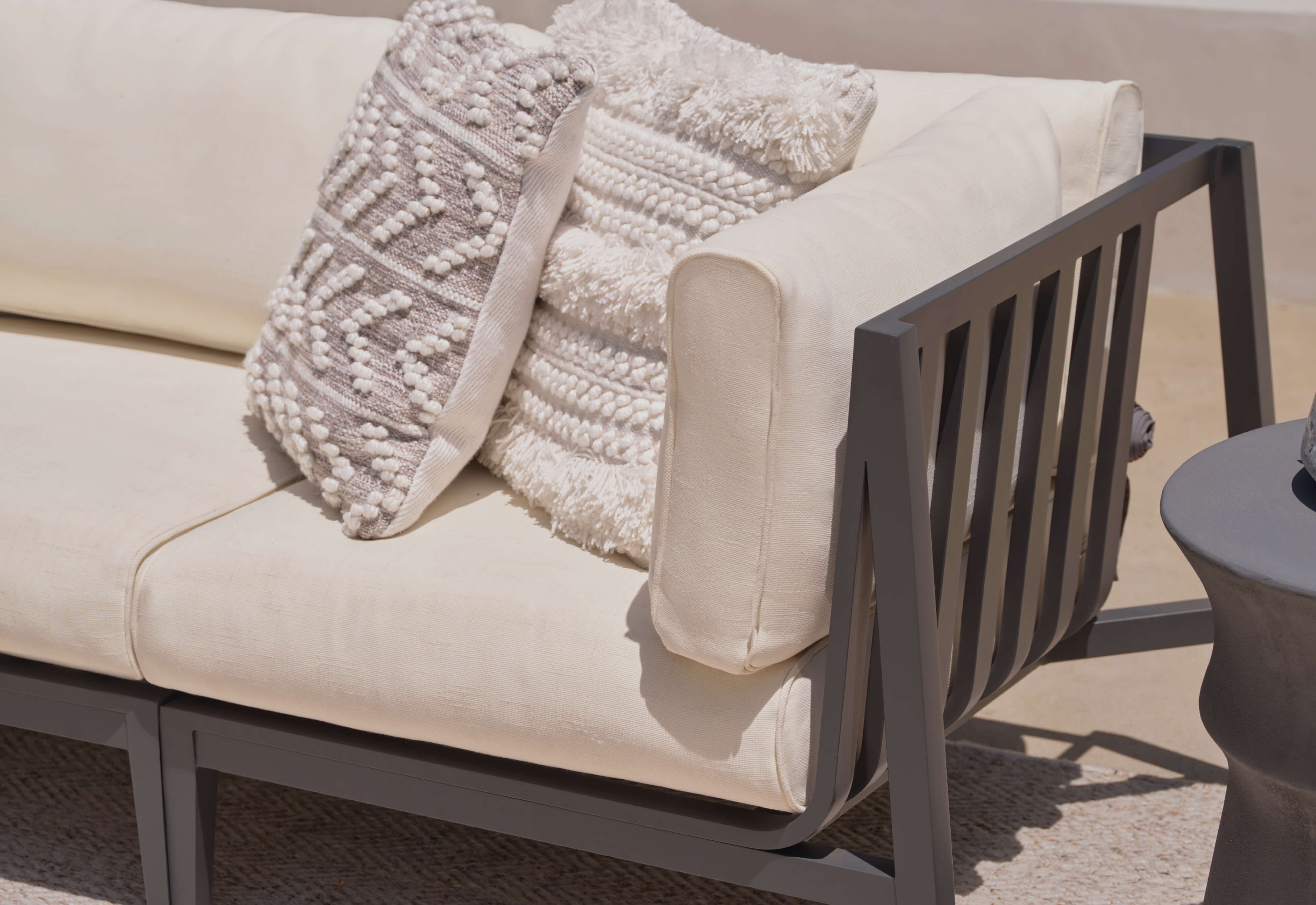 Charcoal aluminum loveseat with palisades cream cushions at an angle.