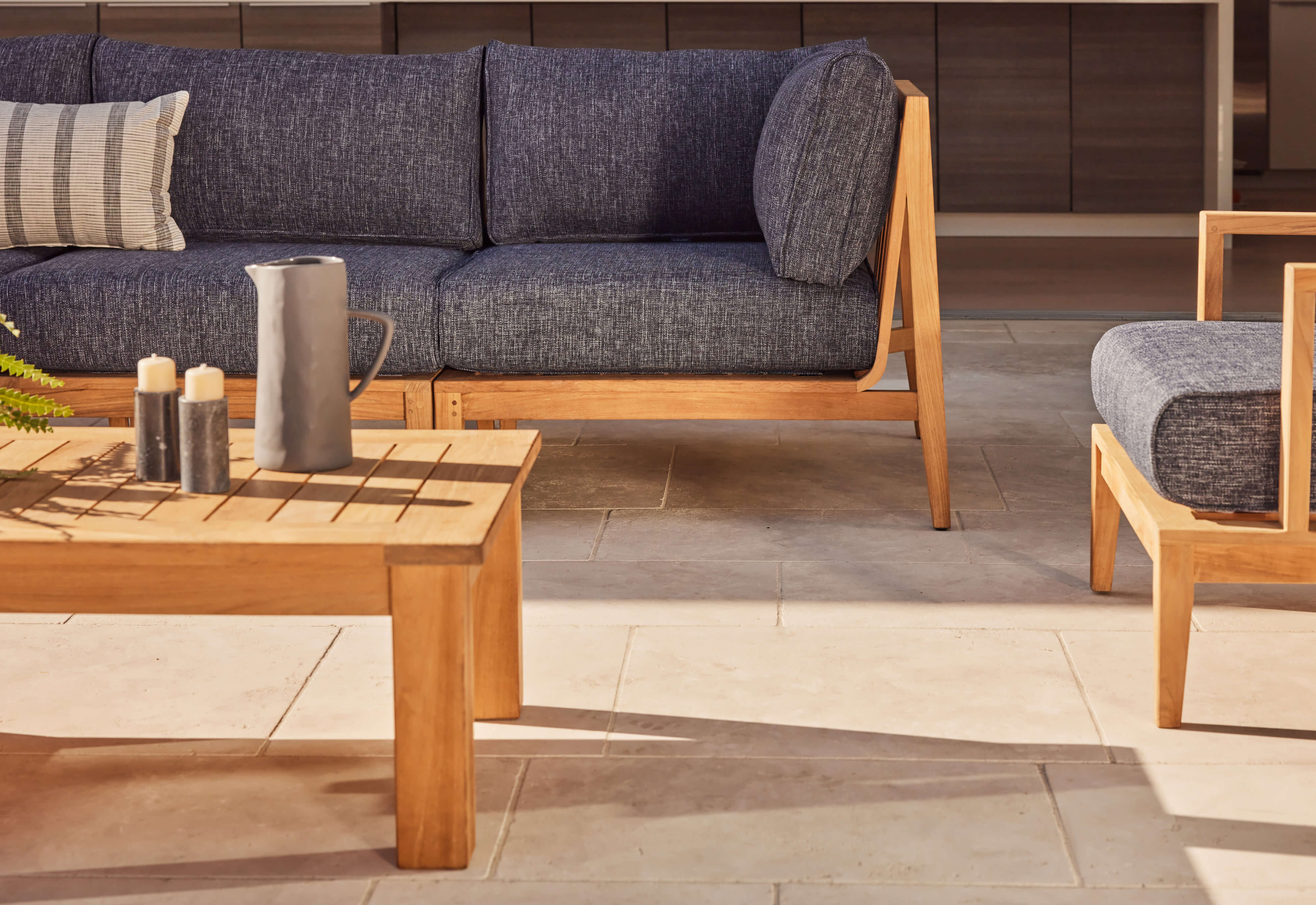 A teak outdoor sofa with matching armchairs, featuring navy cushions and a sturdy wooden frame, arranged on a patio.-teak outdoor sofa-outer