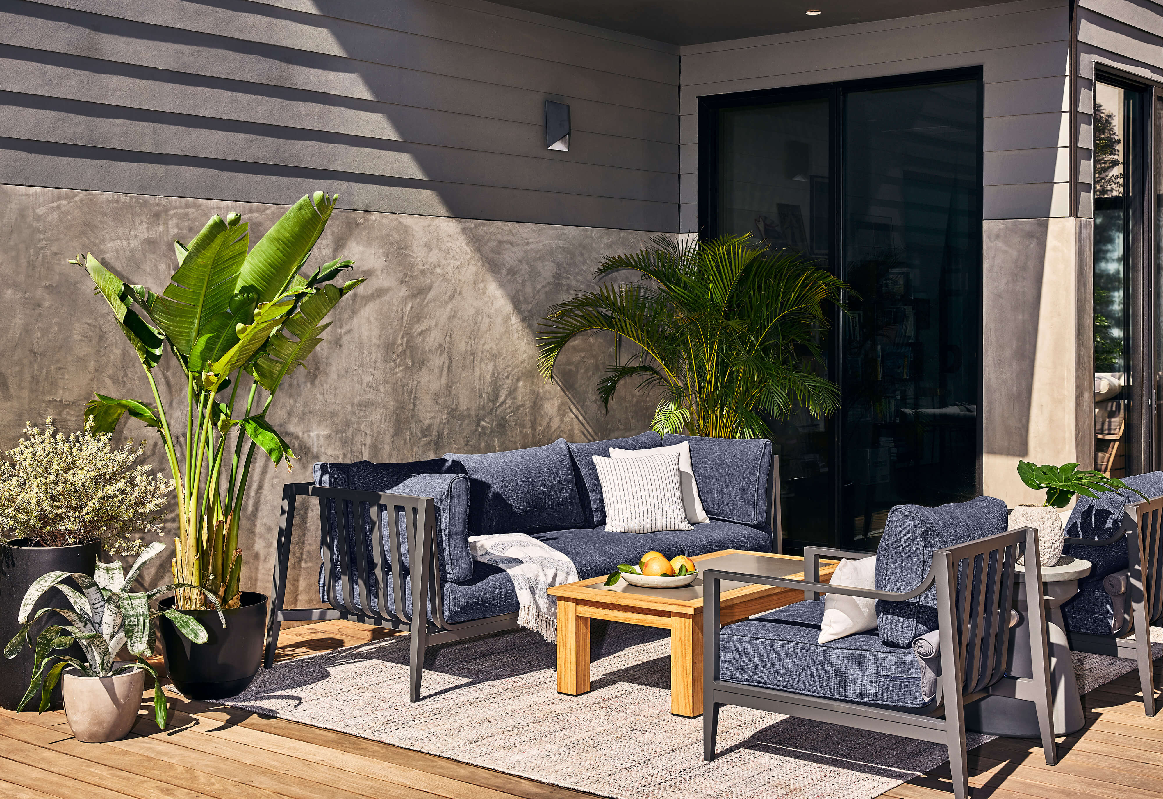 Eco-Friendly Outdoor Rug in Sand Dune Beige shown in a backyard with Outer's outdoor aluminum sofa in Navy fabric.