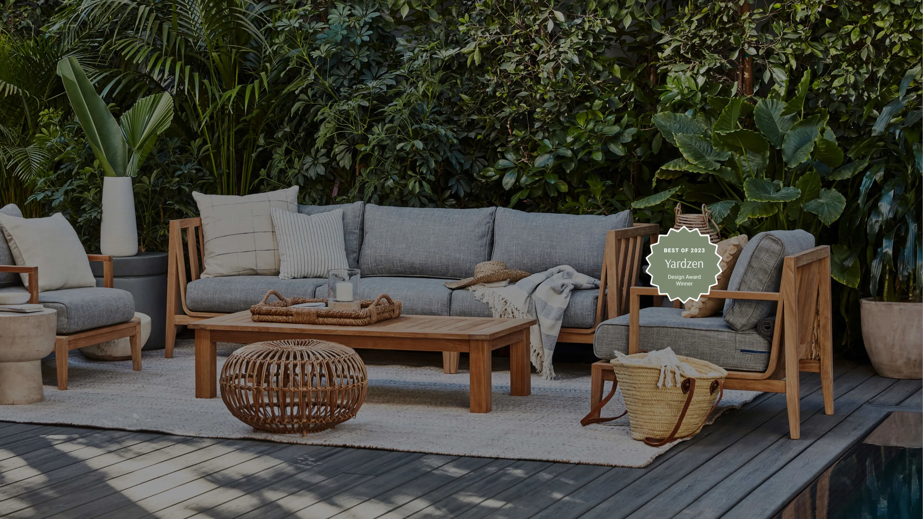 Teak outdoor sofa with gray cushions arranged on a patio with a wooden coffee table and lounge chair
