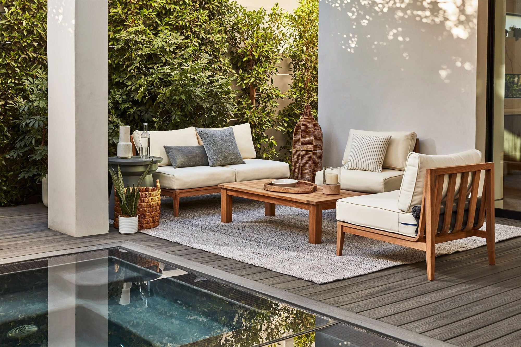 Teak outdoor sofa with two armless chairs and white cushions arranged on a wooden deck.-teak outdoor sofa-outer