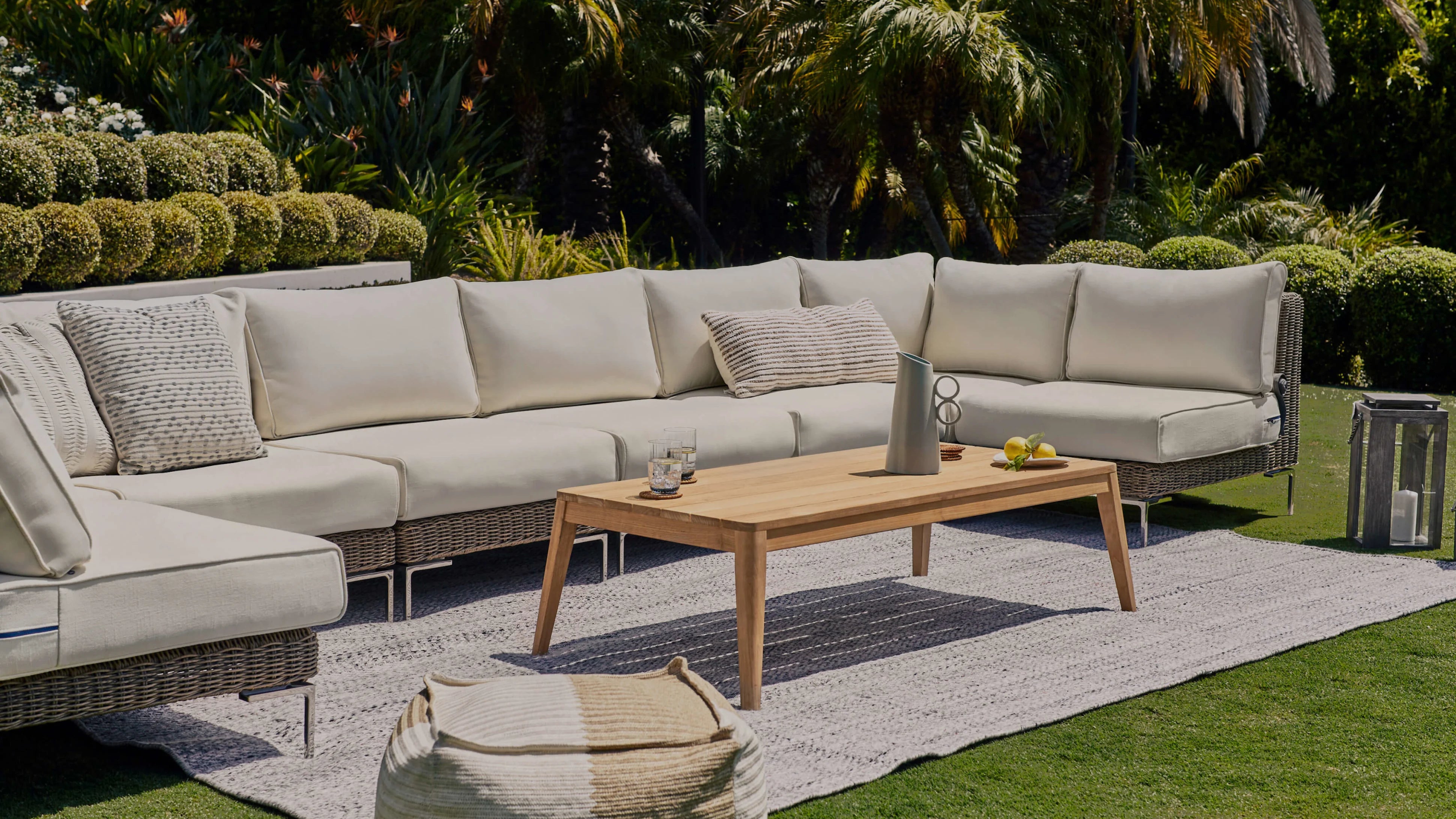 Wicker outdoor sectional sofa with light cushions arranged on a patio with a wooden coffee table and rug
